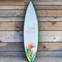 Load image into Gallery viewer, Surfboard with birds of paradise design for a tropical beach themed wedding against a wooden wall
